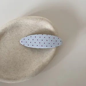 Gedetailleerd macro-aanzicht van een blauwe stoffen haarclip met rode stippen op een plateau