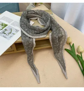 Detalle de un pañuelo de seda gris floral con encaje blanco en soporte de madera.