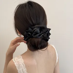 Elegante zwarte satijnen scrunchie met gelaagde ruches op een laag knotkapsel.