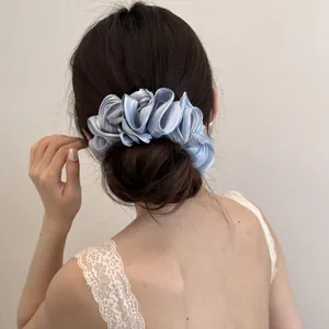Elegante parelmoerblauwe satijnen haarelastiek met laagjes gedragen op een haarknot.