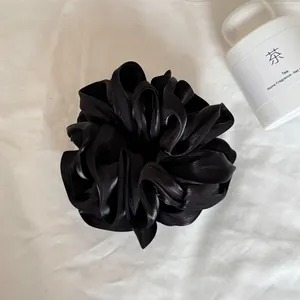 Detailopname van een zwarte satijnen oversized scrunchie met parelglans en gelaagde ruches.