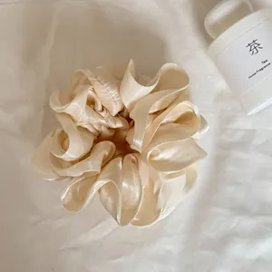 Detail van een beige parelmoer satijnen scrunchie met een elegante gelaagde structuur