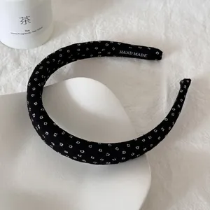 Detail van een zwarte stoffen haarband met witte stippen en handgemaakt label