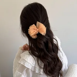Elegant peach mesh bow hair clip styled on long wavy dark hair for a feminine look
