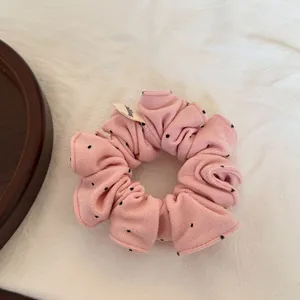 Vue détaillée d'un chouchou rose à pois avec une étiquette de marque sur tissu blanc.