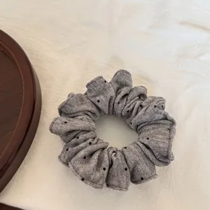 Vue détaillée d'un chouchou en tissu gris plissé avec de délicats petits pois noirs