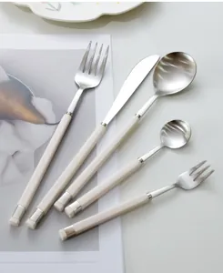 Detail shot of a minimalist 5-piece stainless steel cutlery set with cream handles