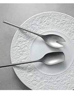 Macro view of 304 stainless steel serving spoons on a textured white ceramic plate.