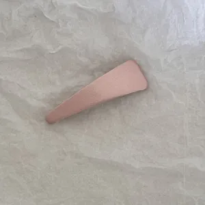 Gros plan d'une barrette à cheveux rose recouverte de tissu sur un fond texturé neutre.