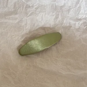 Gros plan d'une pince à cheveux BB en tissu vert sur un fond de papier beige texturé et froissé.