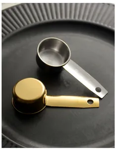 Silver and gold 30ml stainless steel measuring spoons on a black textured plate