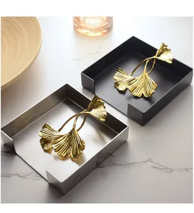 Detail view of square napkin holders with golden ginkgo leaf weights on marble