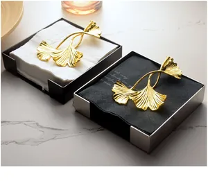 Detailed view of modern stainless steel square napkin holder with gold ginkgo leaf weight