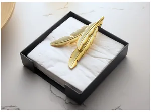 Modern black square napkin holder with golden feather weight on marble surface