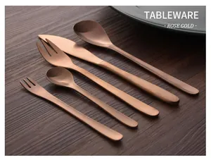 Close-up of a five-piece rose gold stainless steel cutlery set arranged on dark wood surface
