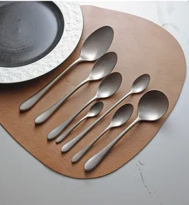 Set of vintage matte silver stainless steel spoons arranged on a brown leather mat