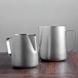 Two professional 304 stainless steel milk frothing pitchers displayed on a wooden table