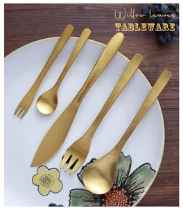 Detail of gold stainless steel cutlery set with willow leaf design on a ceramic plate