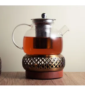 Detailed view of a vintage bronze tea warmer with glass teapot on a wooden base