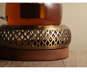 Detail view of retro stainless steel tea warmer with glass teapot on solid wooden base.