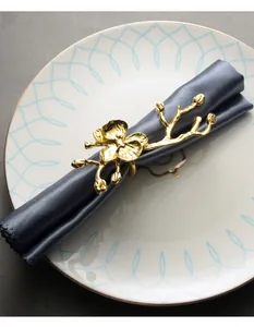 Detalle de un servilletero floral dorado sobre servilleta gris y plato decorativo