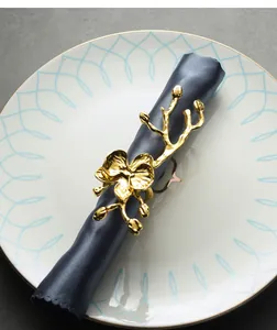 Detalle de servilletero dorado con forma de orquídea sobre una servilleta azul oscuro