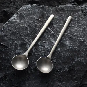 Two vintage Japanese style handmade metallic coffee mixing spoons on textured volcanic rock
