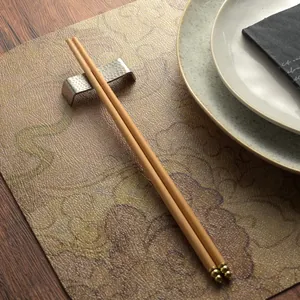 Premium Chinese wooden chopsticks with golden tips and a hammered metal rest for dining