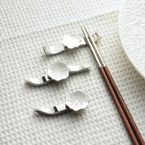 Elegant 304 stainless steel floral chopstick rests with wooden chopsticks on a white cloth.