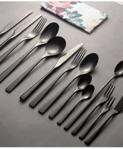Matte black stainless steel cutlery set arranged diagonally on a textured grey surface.