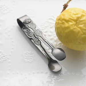 Elegante roestvrijstalen suikertang met rozenreliëf voor koffie op een wit bord.