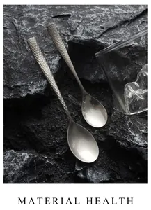 Detailed view of two vintage hammered matte stainless steel spoons on dark rock