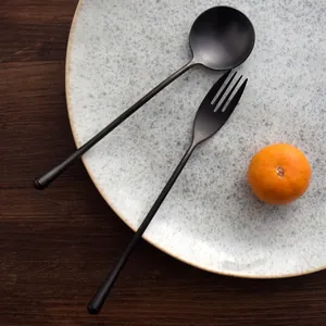 Elegant matte black stainless steel spoon and fork set on a speckled ceramic dinner plate
