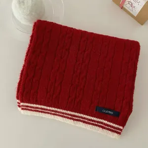 Detailed macro shot of a red cable-knit scarf featuring white stripes and brand label.
