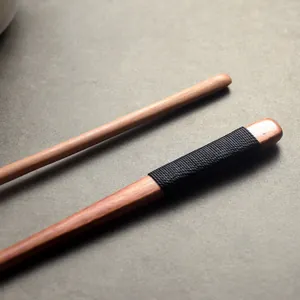 High-quality detailed macro view of long-handle Japanese Nanmu wooden stirrer with black wrap.