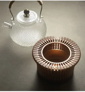 Close-up detail of a vintage bronze hollow tea warmer base next to a textured glass teapot