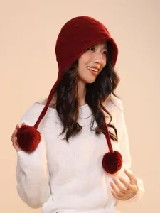 Model wearing red wool knitted elf pumpkin hat with dangling pom-poms in warm studio light