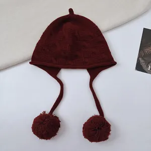 Close-up detail of a burgundy wool knit elf pumpkin hat with soft hanging pom-poms.
