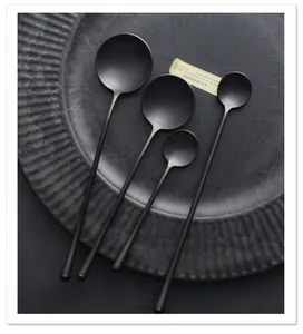 Close-up of four matte black stainless steel spoons in various sizes on a grey plate