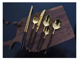 Set of black and gold stainless steel cutlery on a wooden board featuring mirror finish