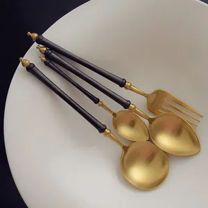 Elegant matte black and gold stainless steel cutlery set with four pieces in a bowl