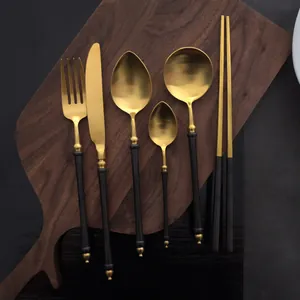 Elegant matte black and gold stainless steel cutlery set displayed on a wooden board
