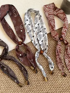 Makroaufnahme von Vintage-Seidenschals mit Paisley-Muster und bernsteinfarbenen Perlen.