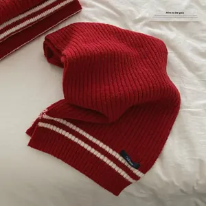 Detail of red knitted scarf with white stripes and dark blue brand label.