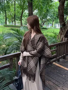 Vrouw die een bruine geruite gebreide poncho met franjes draagt in een weelderig park