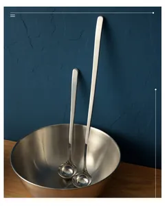 Macro view of long handled stainless steel spoons leaning against a metallic bowl.