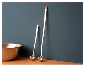 Detailed view of two different sized stainless steel long handle ladles against a blue wall