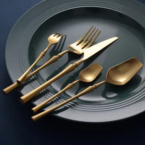 Elegant matte gold stainless steel cutlery set with slim handle design on a green plate.