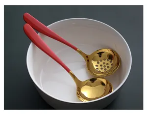 Detailweergave van rode en gouden soeplepel en schuimspaan in een witte kom.