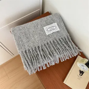 Close-up of a soft and cozy gray mohair knitted scarf with fringes and a lace brand patch